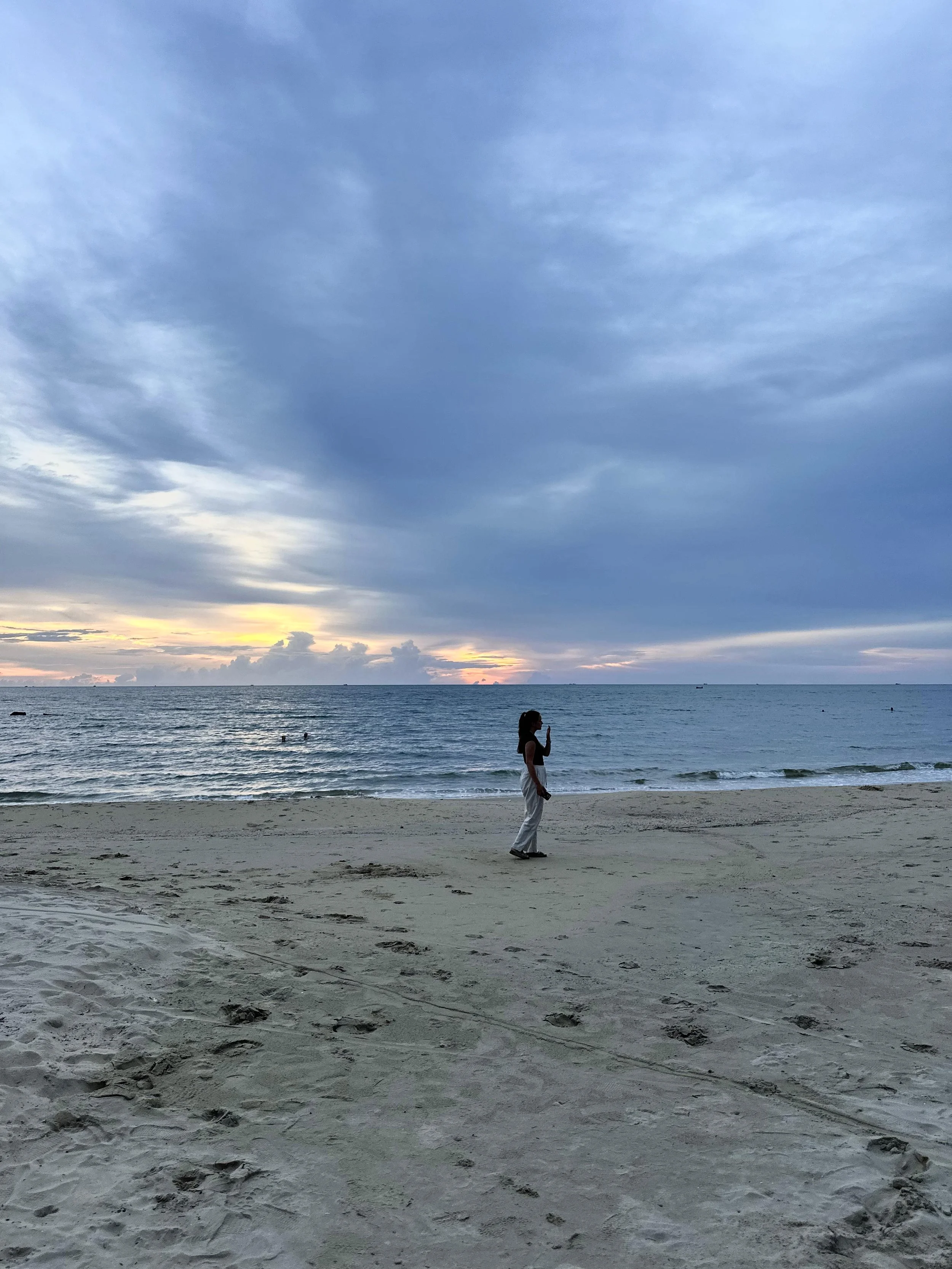 Een persoon staat op het strand bij zonsondergang, kijkt naar de zee, met een blauwe en oranje hemel op Phu Quoc.
