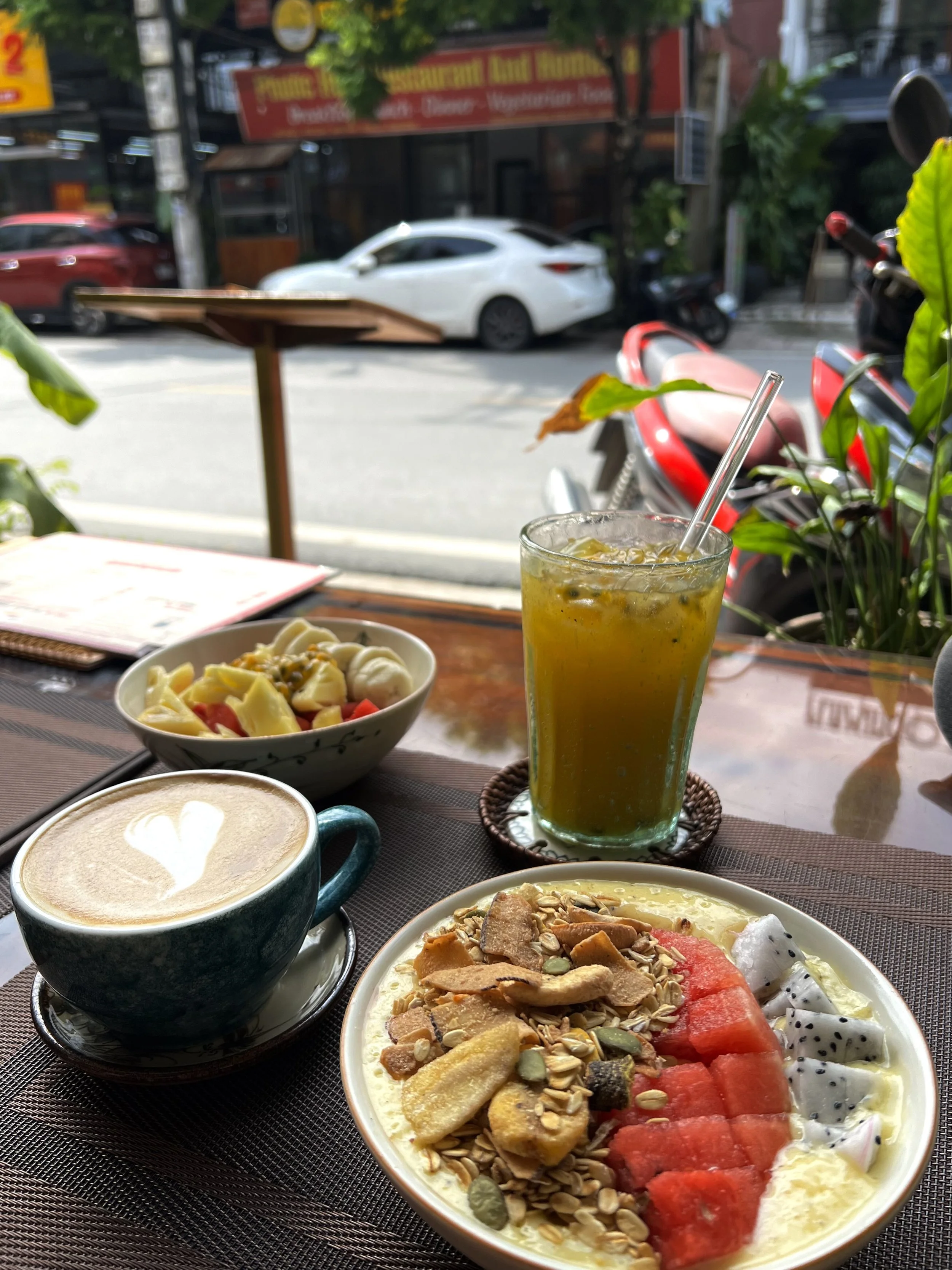 Ontbijt met koffie, vers fruit in een kom, een groene smoothie, en een kom met yoghurt en fruit.