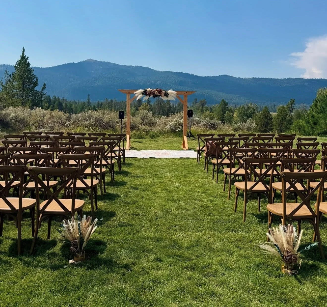 Wedding ceremony with wooden chairs, wedding arch, and mountain in the background