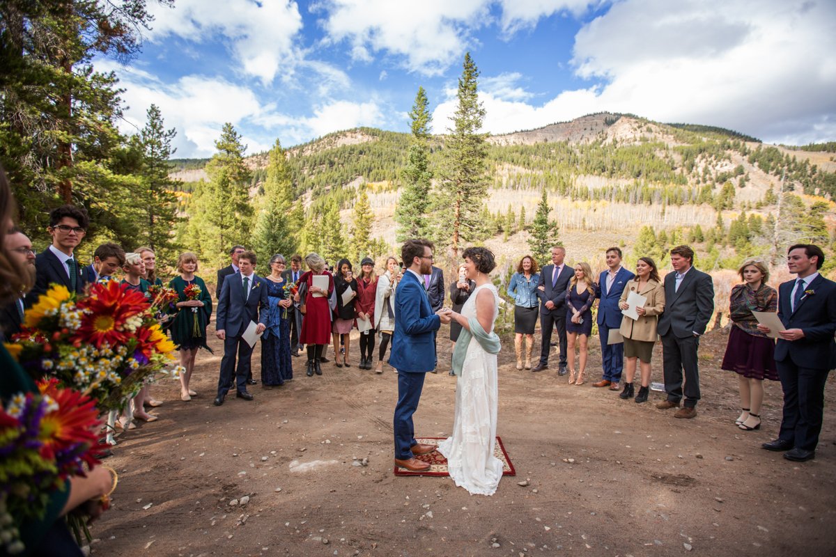 Couple stands on a rug and recites vows to one another while wedding guests circle the couple as witness.