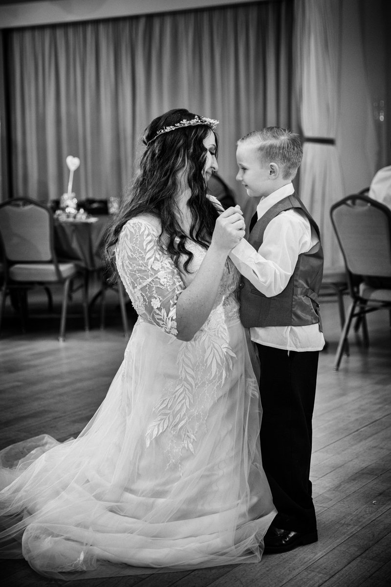 Bride kneels on the dance floor so she can dance with a young child.