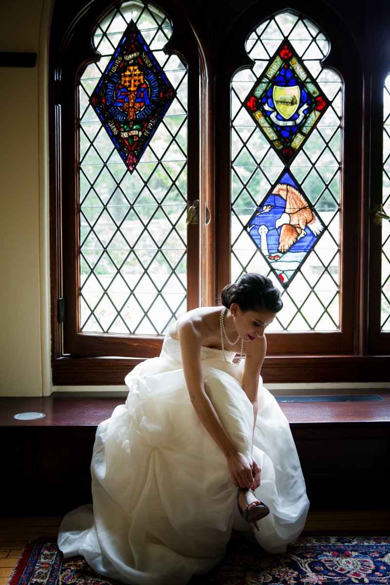 A bride puts on her shoes in front of stained glass windows