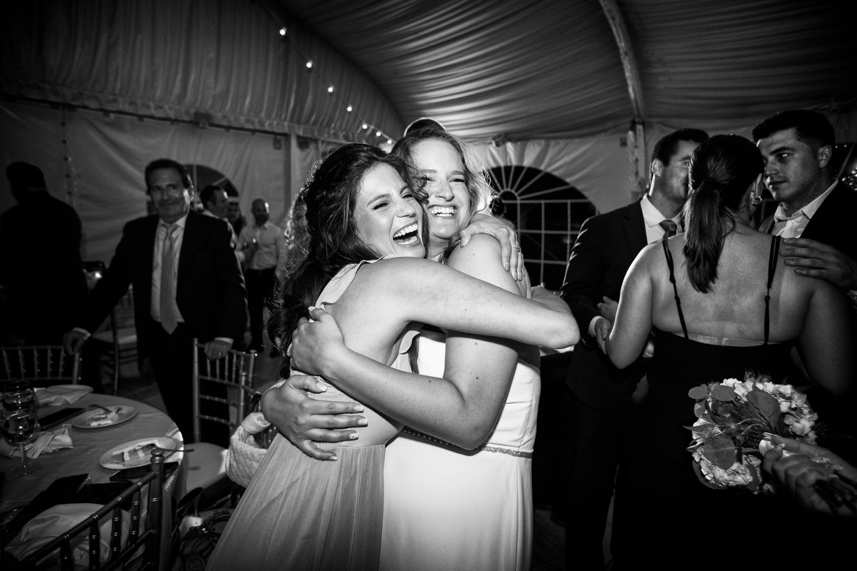 Fun party photo in black and white of a bride and her friend embracing on the dance floor.
