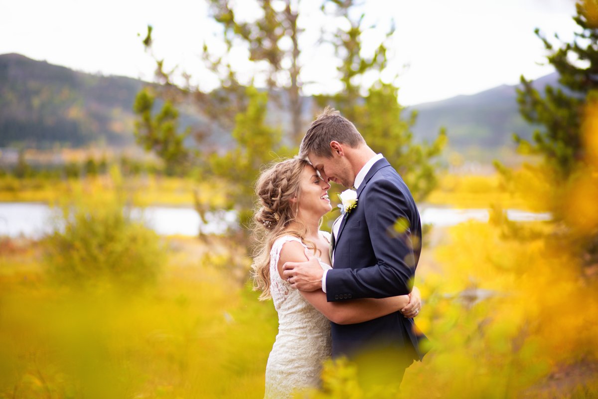 Couple laugh and embrace in the fall foliage with a lake and mountains behind.