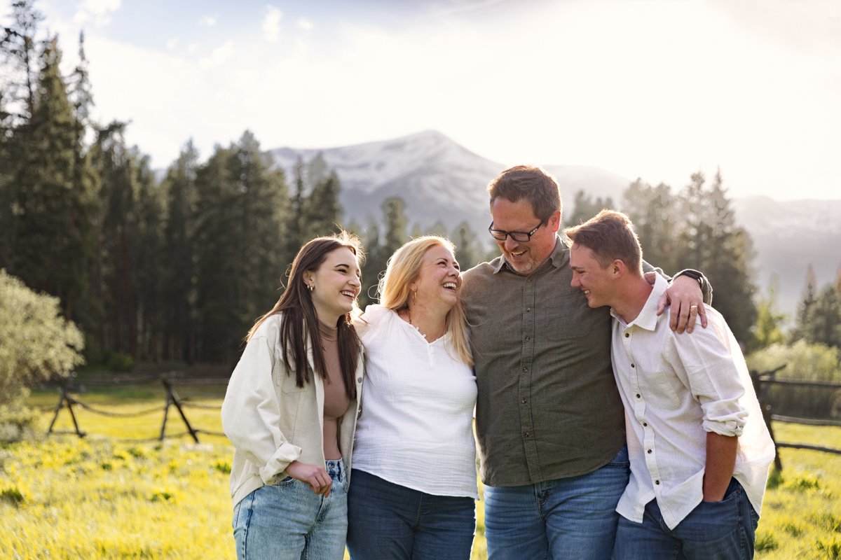 A family of 4 embrace as they stand in field in the mountains.