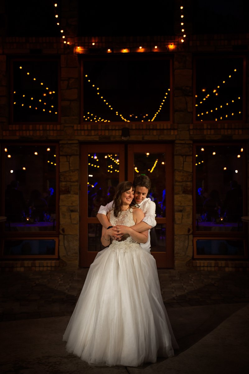 Night portrait of a couple embracing under cafe lights that are also reflected in glass doors behind them.