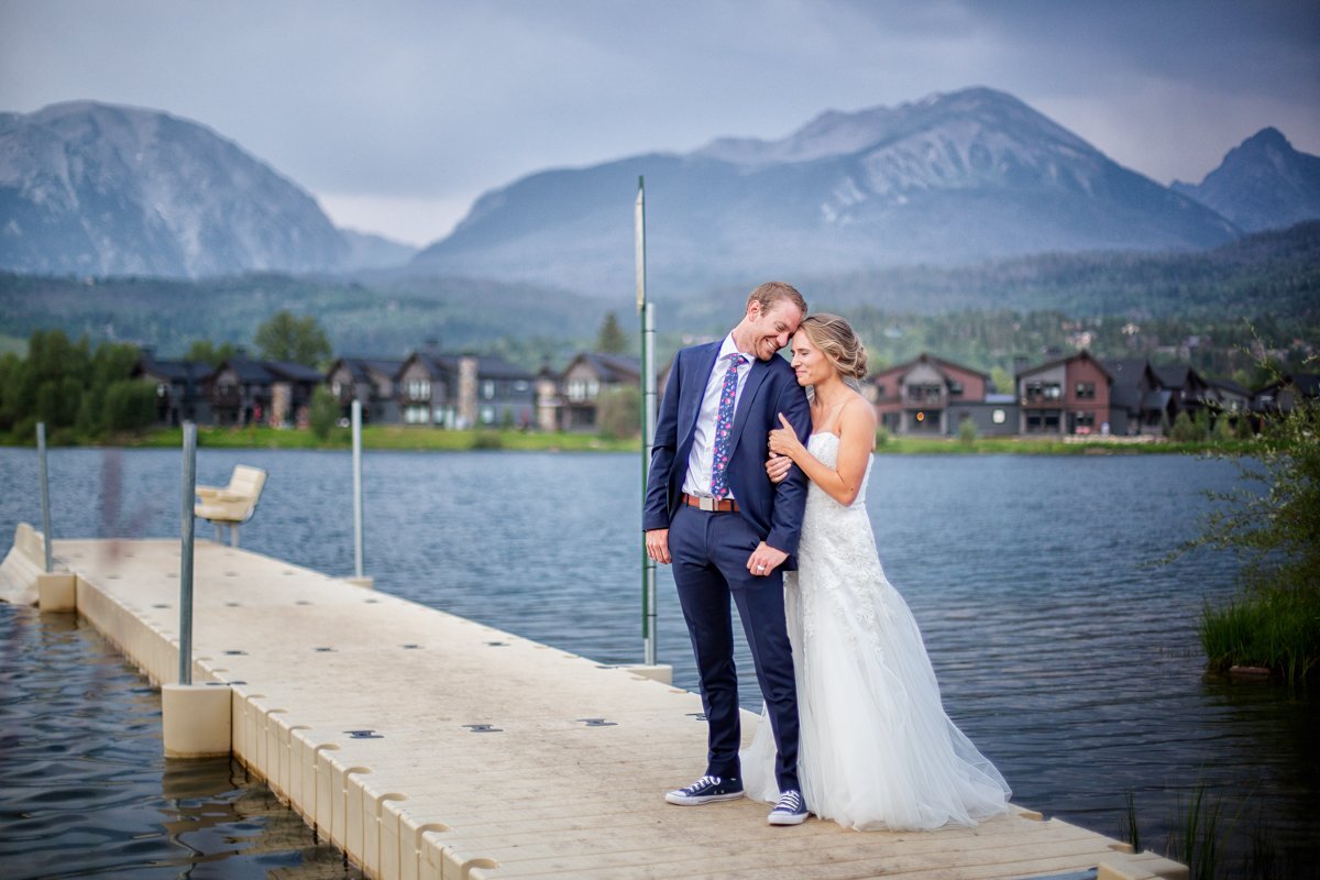 Couple embrace on a dock in Silverthorne Colorado. Groom has a suit on with chucks and bride is in a simple white dress. It's blue hour/dusk.