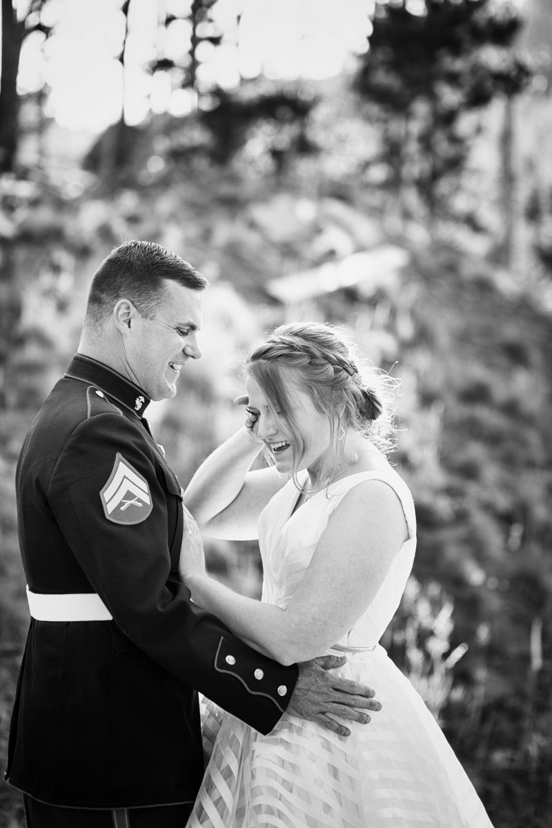 Bride cries happy tears as the husband in military uniform holds her.