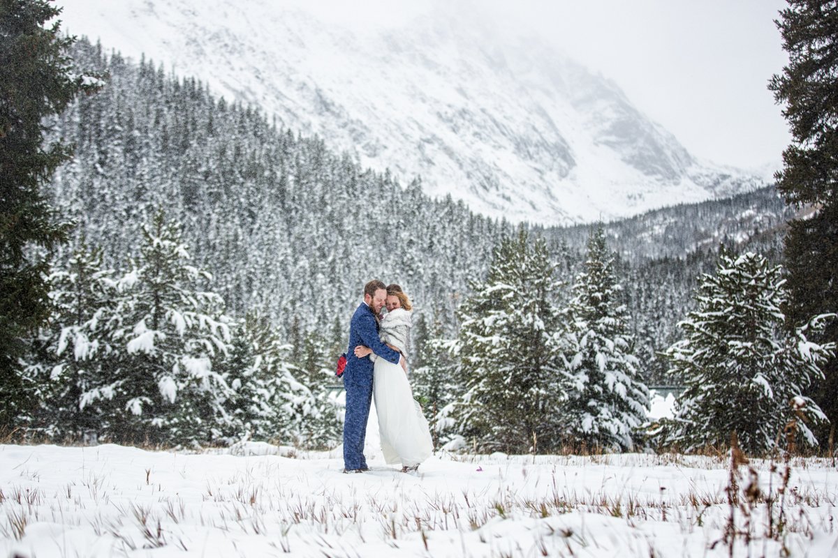 Couple huddle together as a large gust of snowy wind blows in front of the famous 14er Quandary Peak.