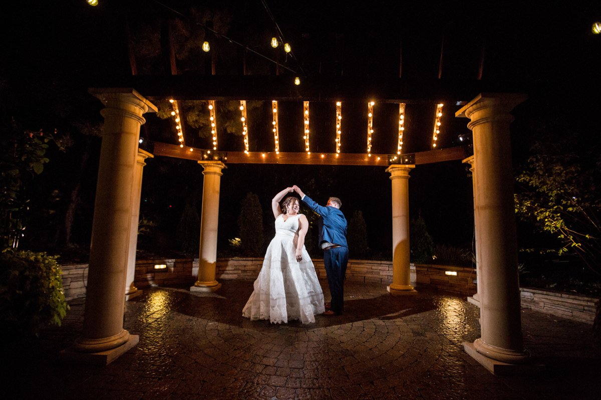 Couple dancing under a lit pergola at night.