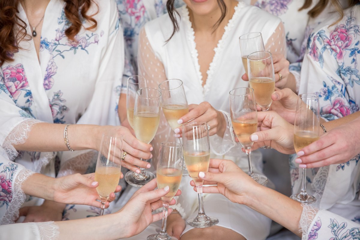 close up shot of bridesmaids doing a cheers with champagne in their floral coordinating robes.
