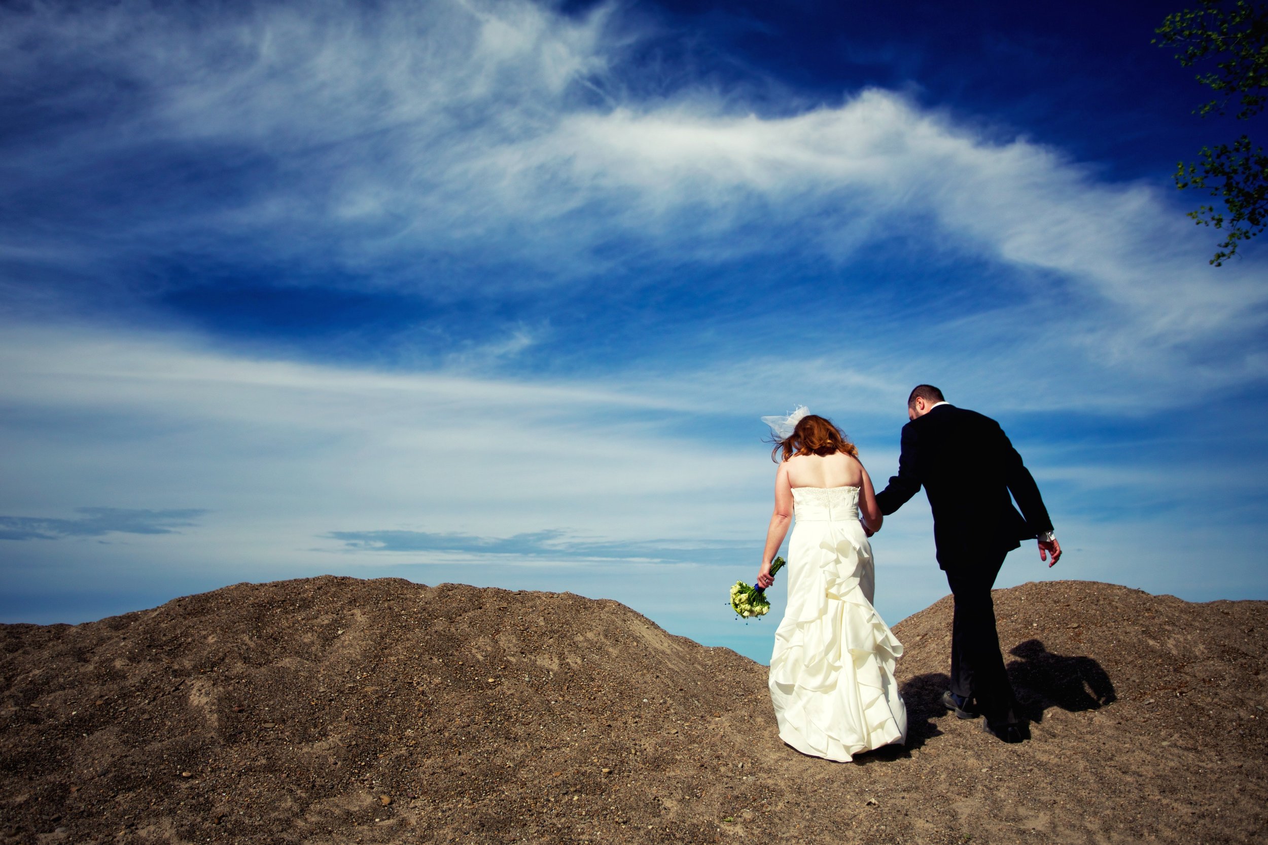 Couple walk hand in hand over sand dunes with a vibrant blue sky.