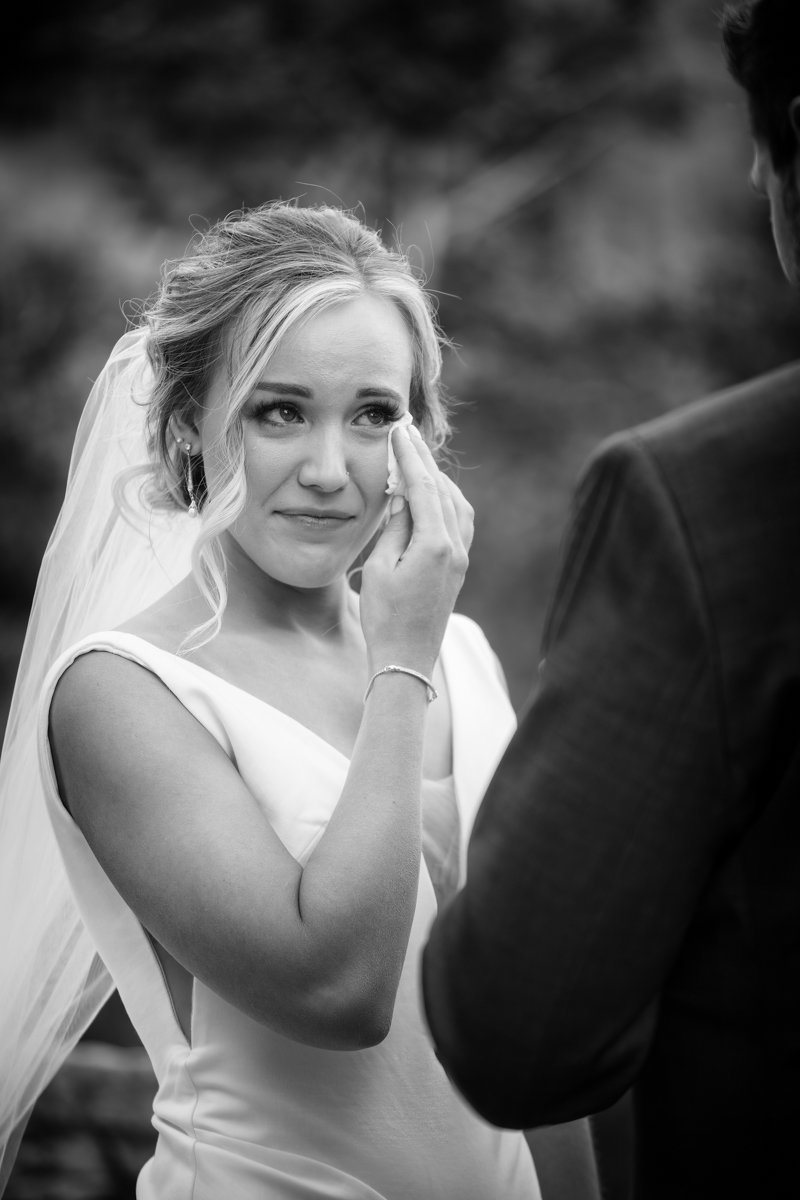 Bride wipes a tear as groom recites vows to her. Black and white image.