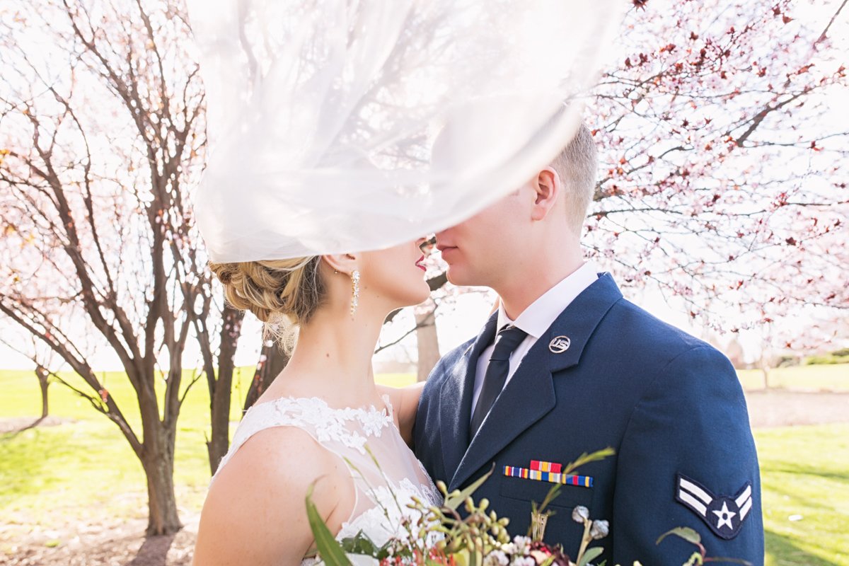 bride and groom almost kiss but wind has blown her veil toward the camera obscuring the top half of their faces.