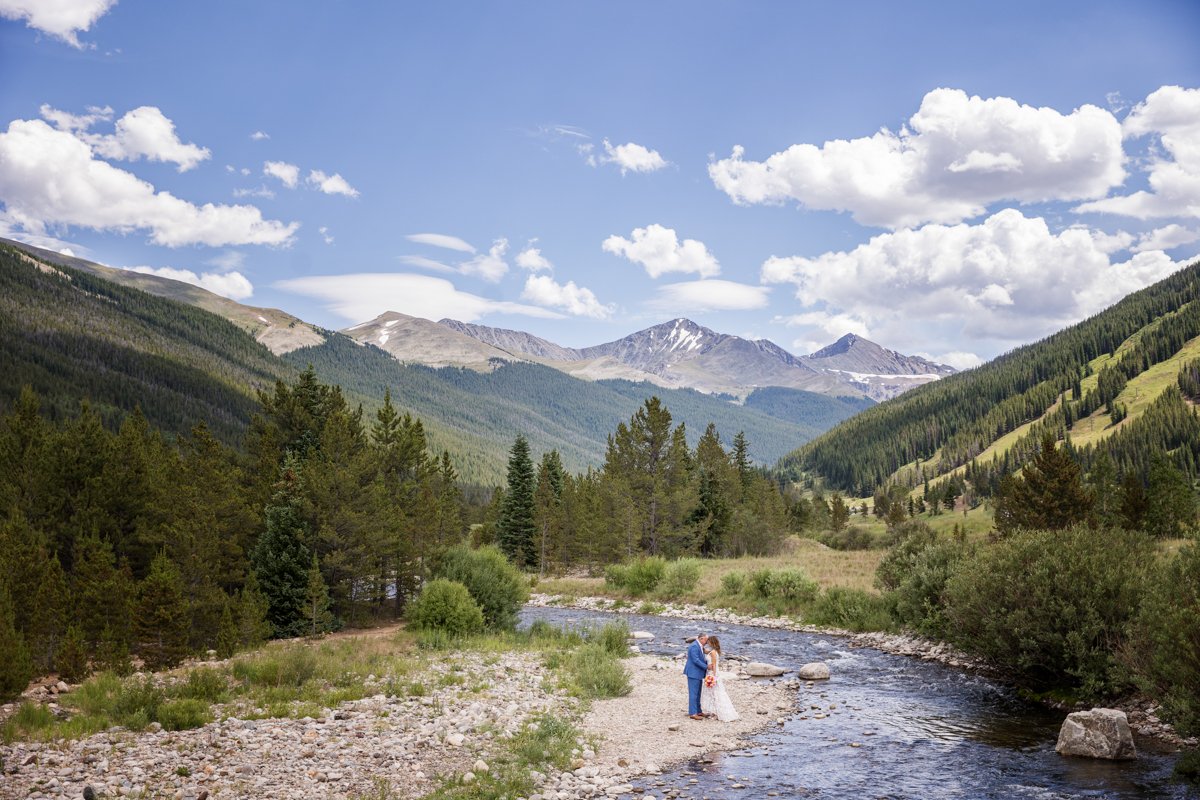 A couple along the shore of a mountain stream surrounded by peaks. Wide angle view.