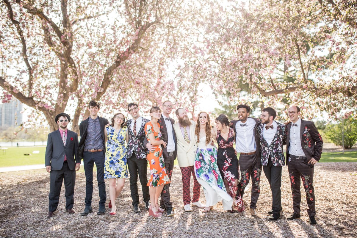 Wedding party dressed in mismatched florals under pink flowering trees in spring.