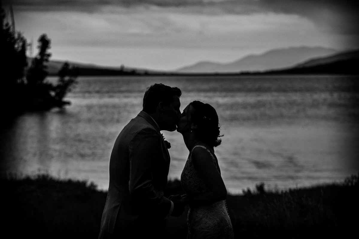 Couple kiss in black and white silhouette with the lake and mountains behind