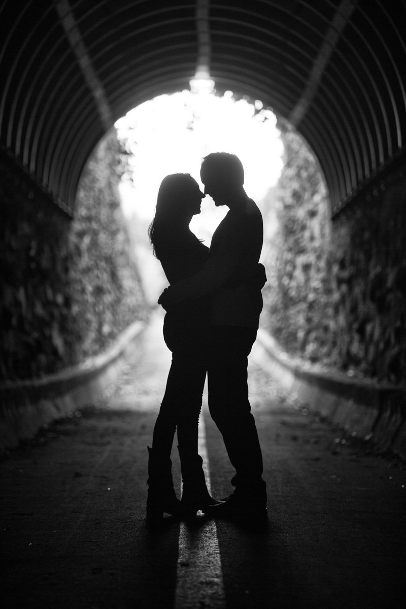 Silhouette photo of a couple, in profile, in the opening of a tunnel.