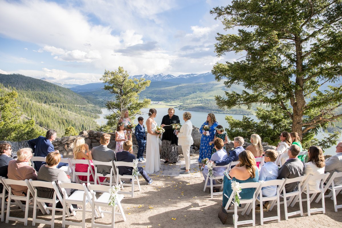 Two brides share vows with family seated around them at Sapphire Point on a beautiful summer day.
