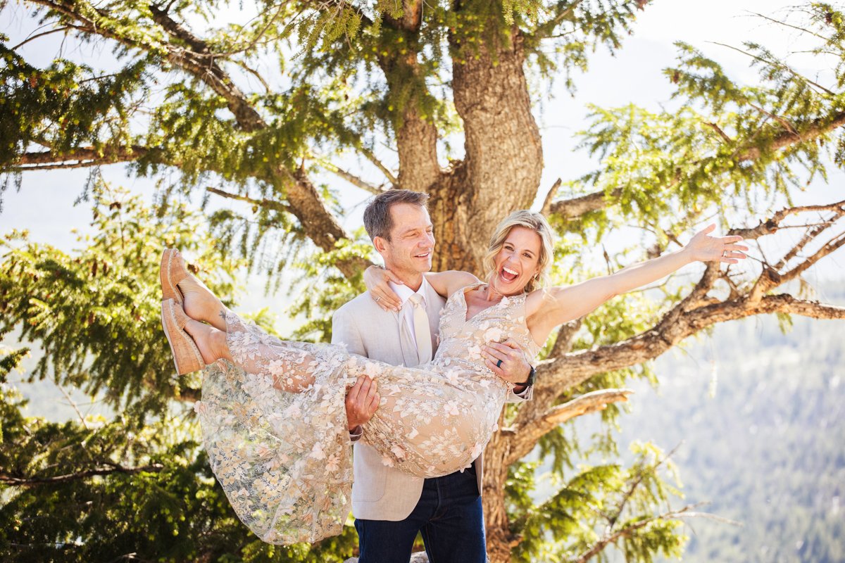 A groom picks up his bride who is wearing a champagne embroidered dress and she is cheering after their vows.
