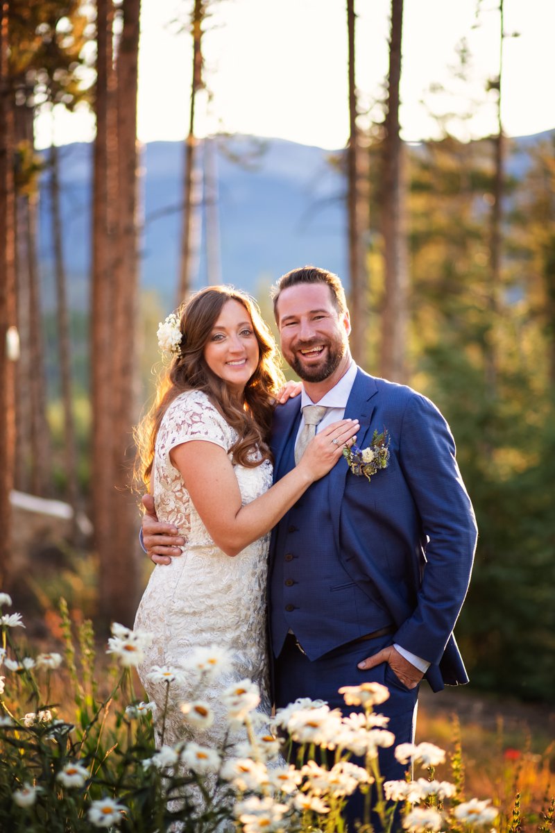 Couple standing in daisys at sunset smiling at the camera.
