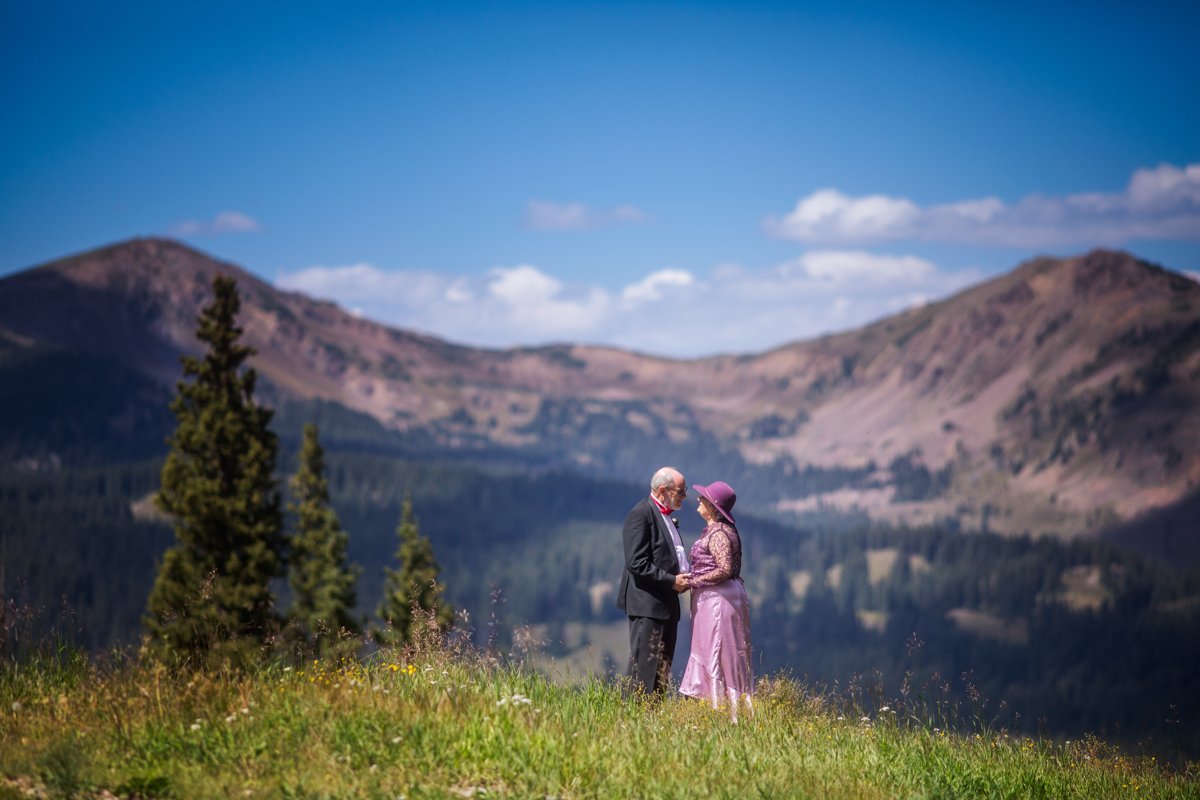 Mature couple stand atop Copper Mountain wearing purple hues before their wedding ceremony.
