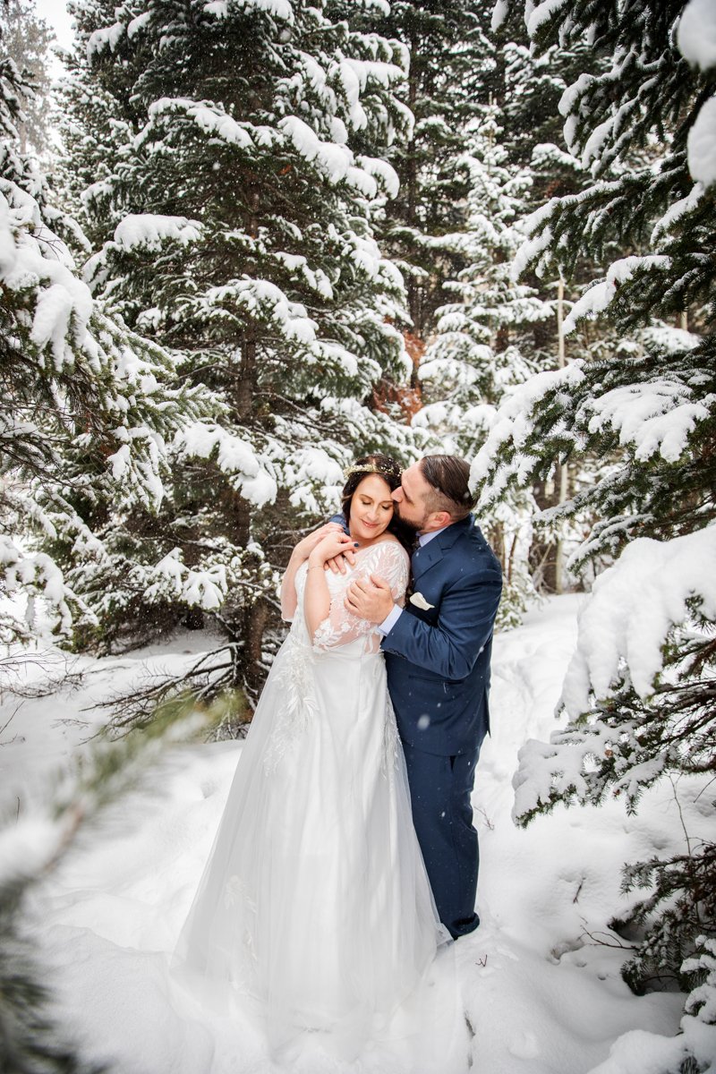 couple embrace in very snowy evergreen forest