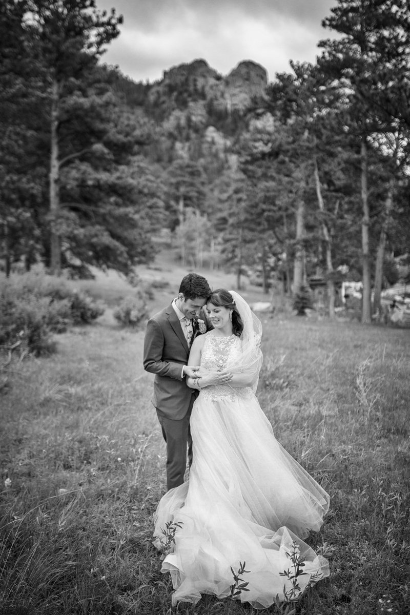 Couple embraces in a field in Estes Park. Bride's dress blows in the wind.