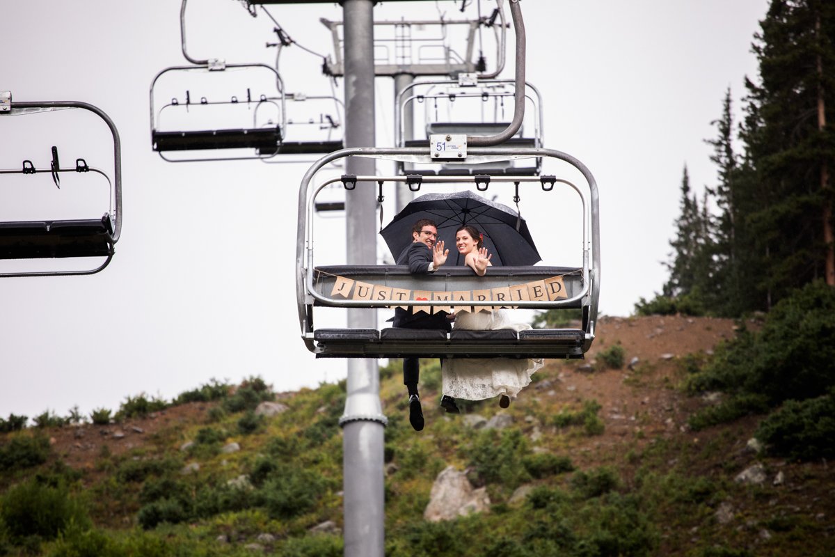 Couple on a ski lift looking back at the camera and waving. "just married" sign hanging on their chair lift.