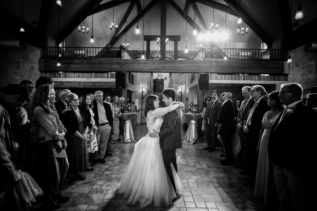 Dramatic first dance photo of a couple in black and white with the dance floor lined with friends and family.