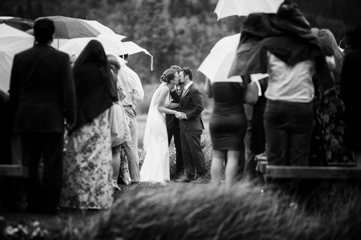 Couple kiss during their ceremony in the pouring rain. black and white.