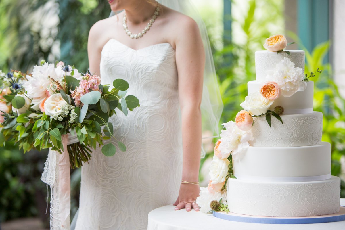 Detail shot of a bride standing next to her cake while holding her flowers. The soft pink and peach colors are coordinated.