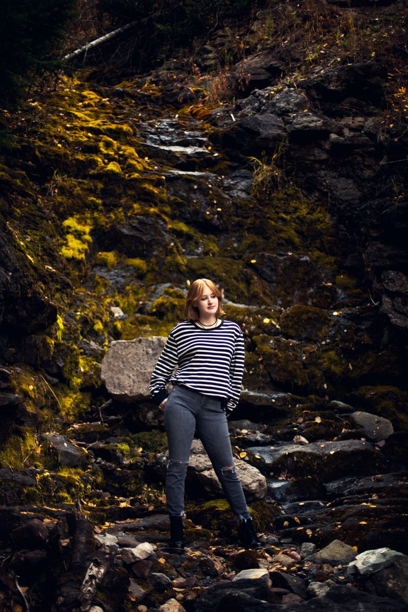 A young woman stands in a dried up waterfall rock wall.