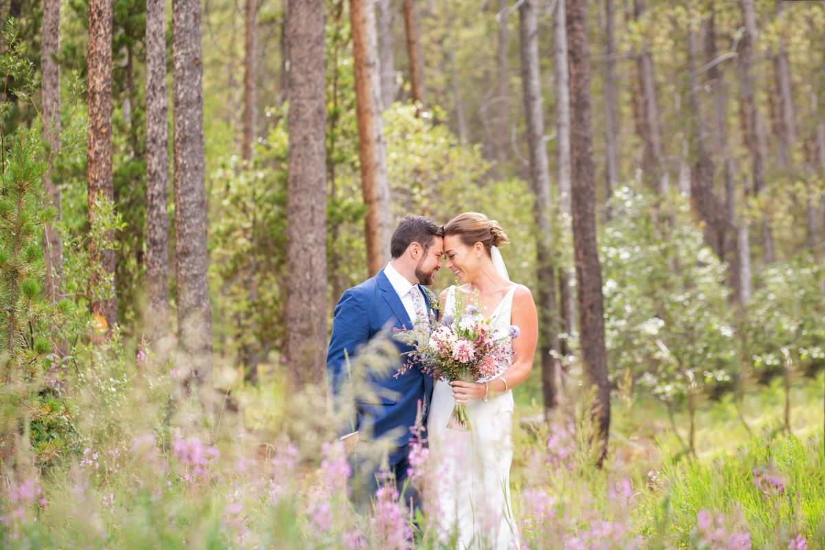Bride and groom having a quiet, snuggled moment in a field of wildflowers in the forest.