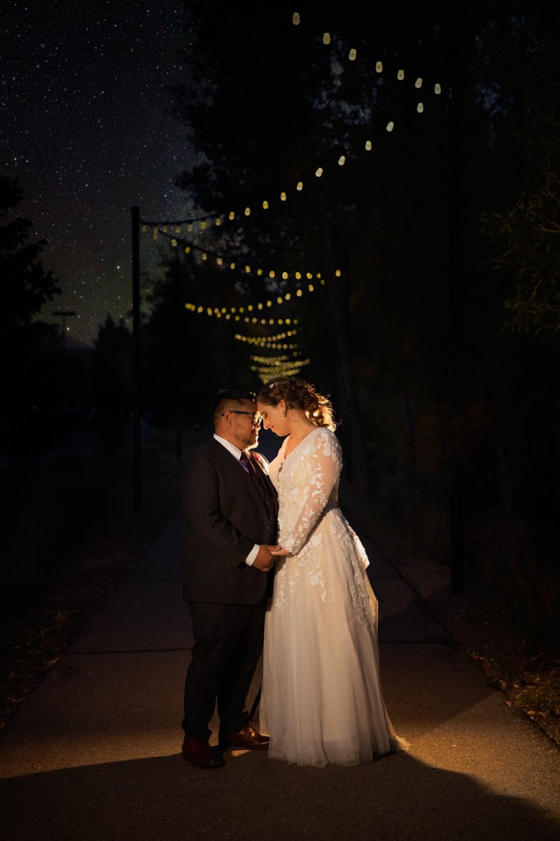 Couple stands outside at night under string lights with stars in the sky.