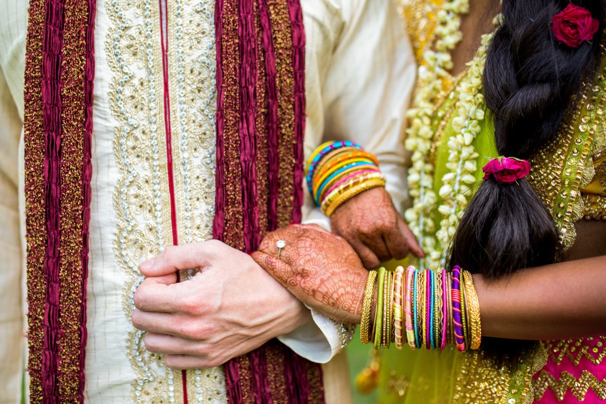 Close up detail photo of an Indian wedding couple standing with linked arms. The shot shows off the intricate beading and elaborate jewelry of the Indian wedding ceremony.