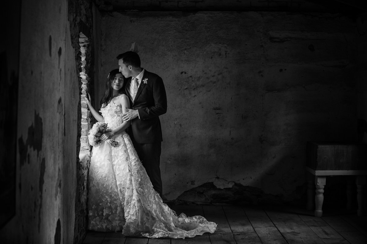 Couple stand next to a window in an old building with crumbling plaster walls.