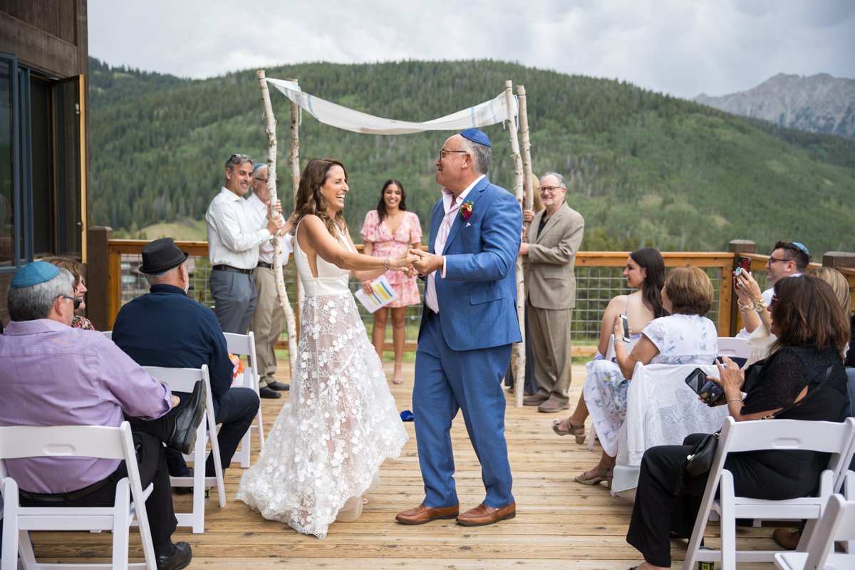 A couple dances down the aisle after they complete their ceremony. A Chuppah held by family members is behind them.