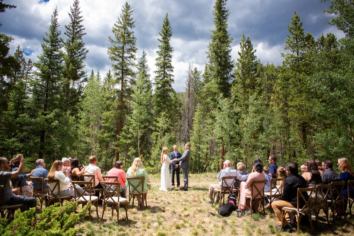 Couple say vows in the forest with guests sitting in chairs around them.