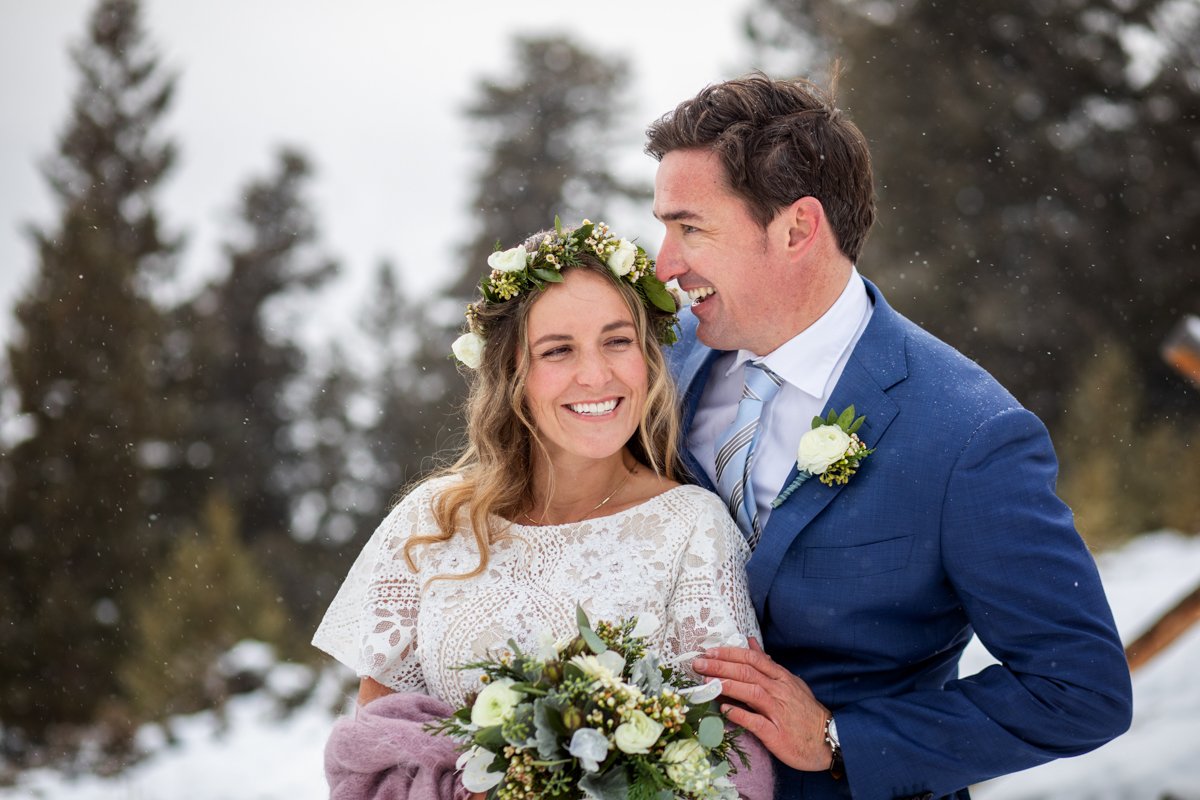 Couple smiles as snow falls around them.