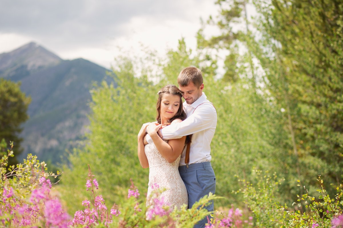 A couple in wedding attire embrace in the spring wildflowers with a large mountain behind them.