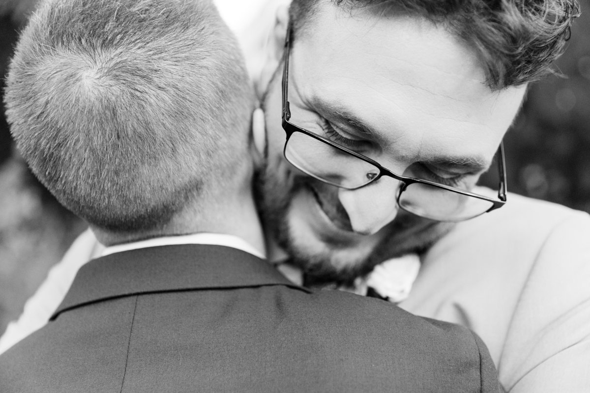 Two grooms embrace. Close up over the shoulders of one. Black and white.