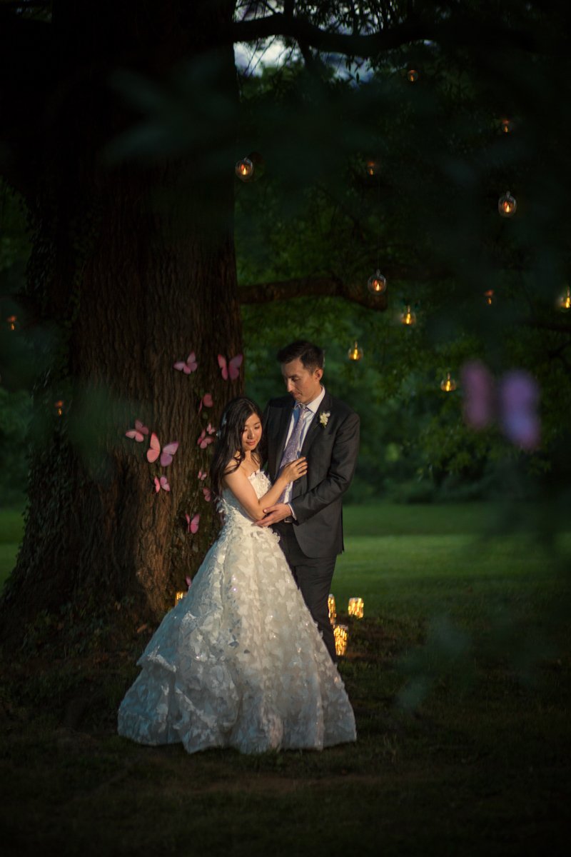 Couple under a tree at dusk with twinkling lights that look like fireflies.