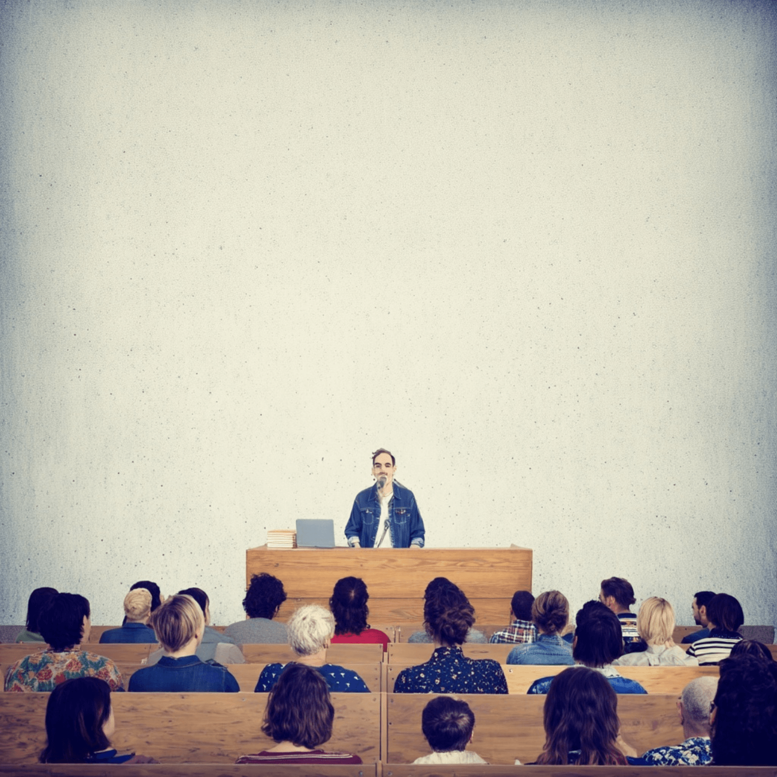 Een man staat achter een houten spreekgestoelte voor een publiek in een auditorium.