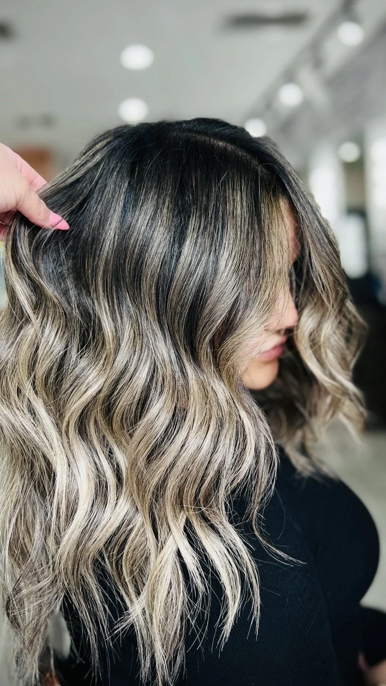 Close-up of a woman's wavy blonde hair being styled or inspected in a salon.
