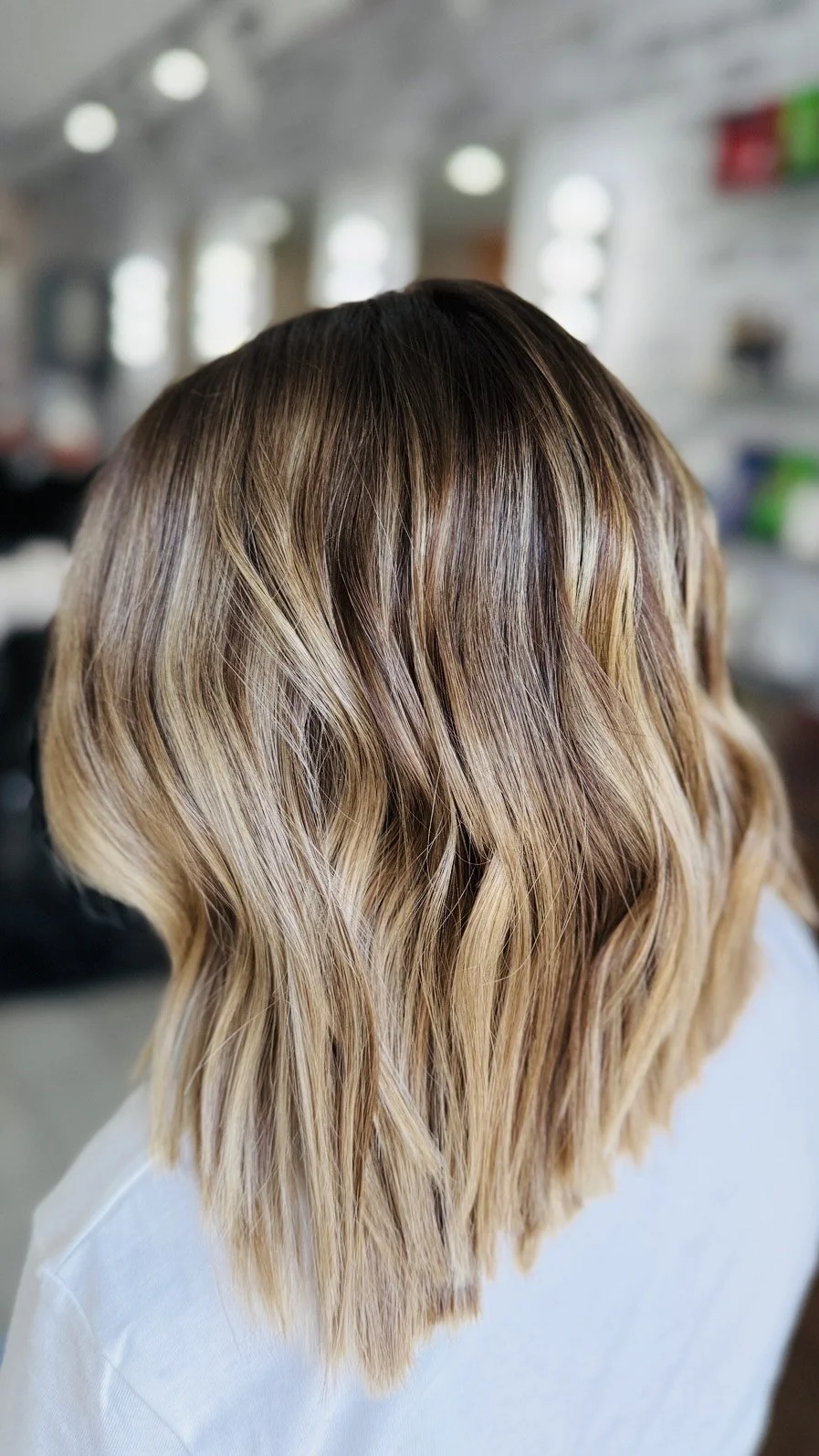 Hair with blonde highlights styled in loose waves, seen from the back in a salon setting.