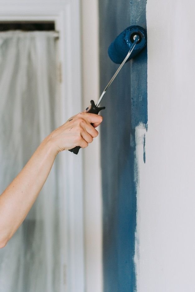 Person painting wall with blue paint roller