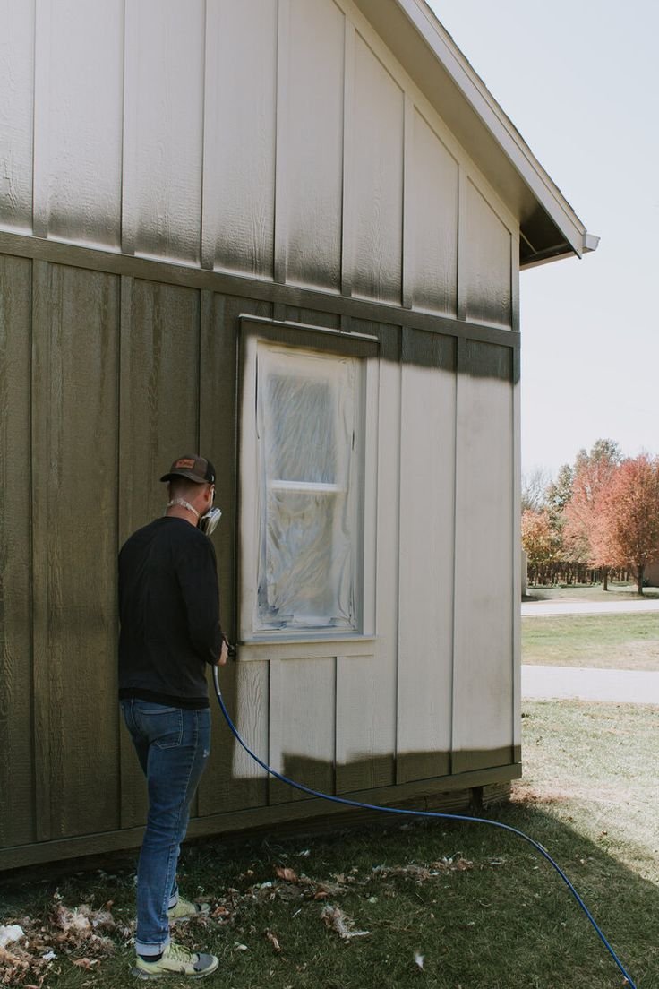 Person painting barn exterior with sprayer