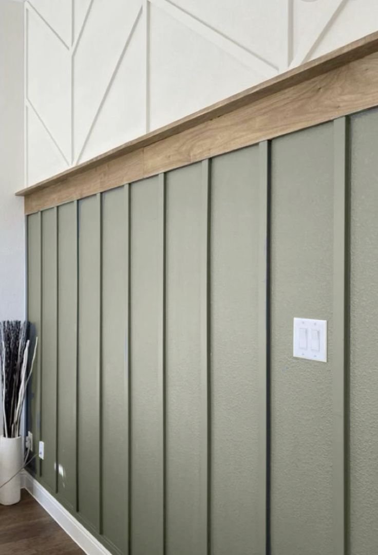 Interior wall with green vertical paneling, decorative wall ledge, white geometric pattern above, light switches, and a vase with sticks.