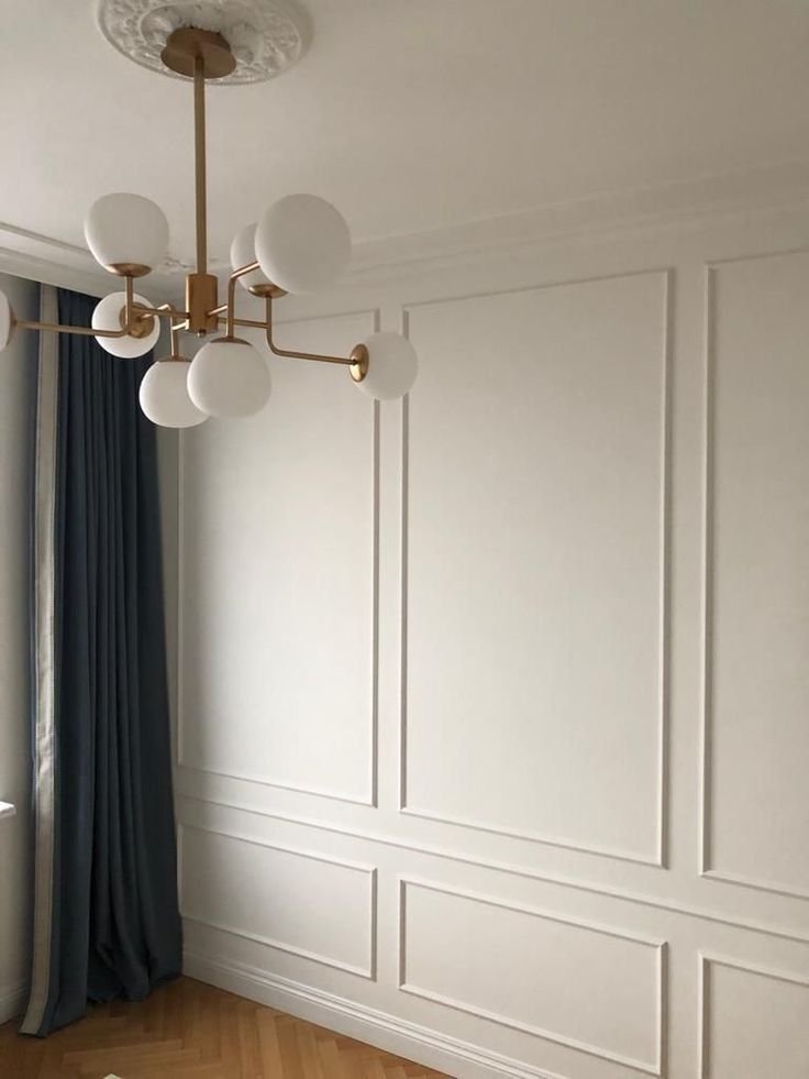 Room with modern chandelier, white paneled walls, and blue curtains